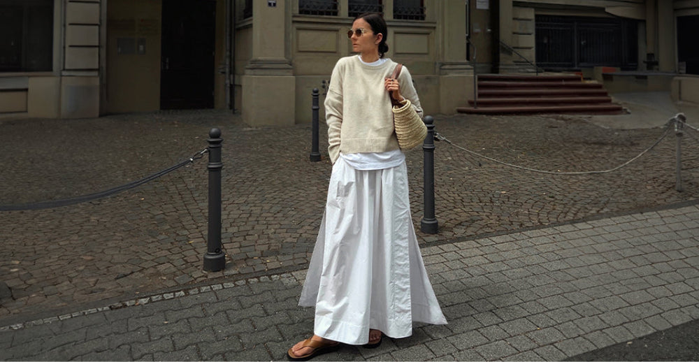 Street-style inspired neutral layering with a cream knit sweater over a white longline tee, paired with a voluminous white maxi skirt and woven tote bag.